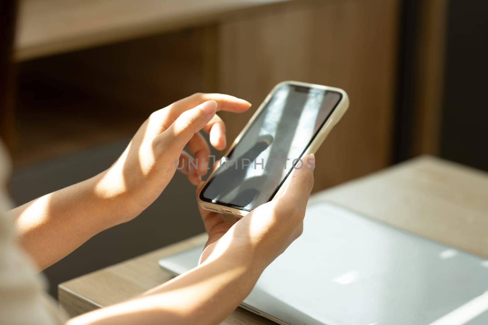 Young woman using mobile phone at coffee table with soft sunlight streaming through the window.