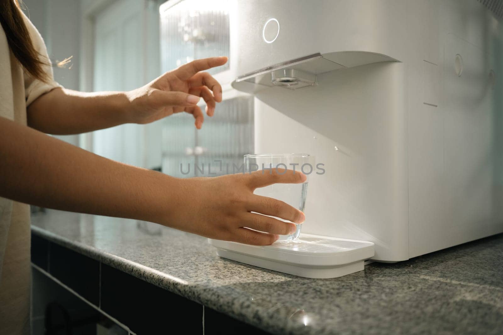 Woman using water purifier marble countertop in a home kitchen. Hydration, health and convenience concept.