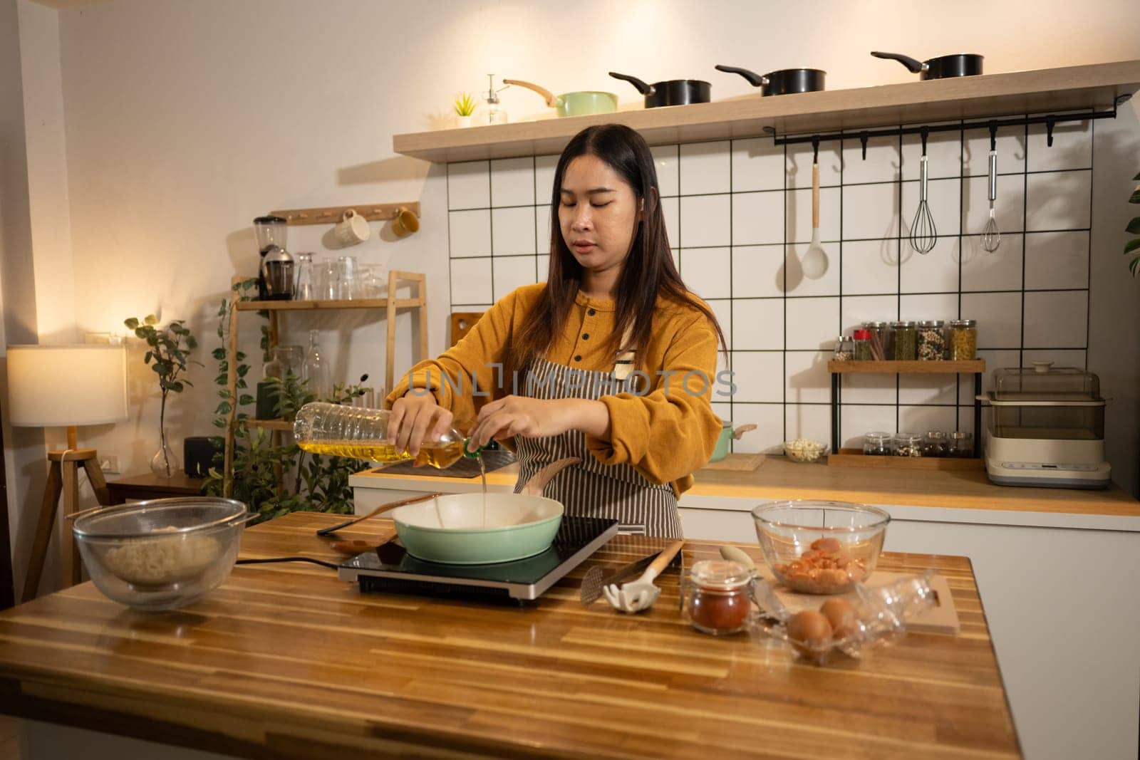 Young woman pouring cooking oil into a frying pan, ready to start the meal preparation.