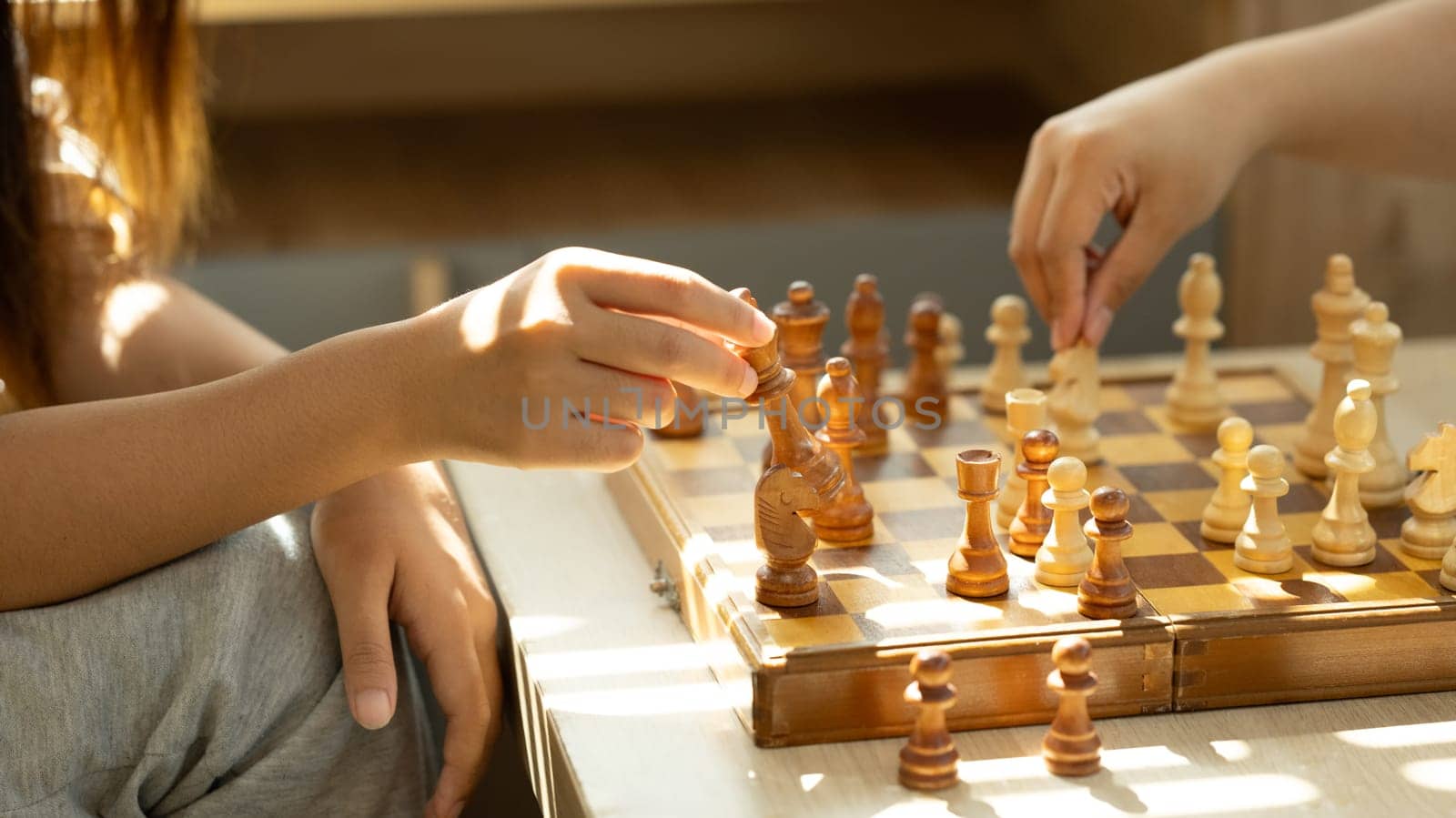 Close up shot of two players playing chess in a sunlit room.