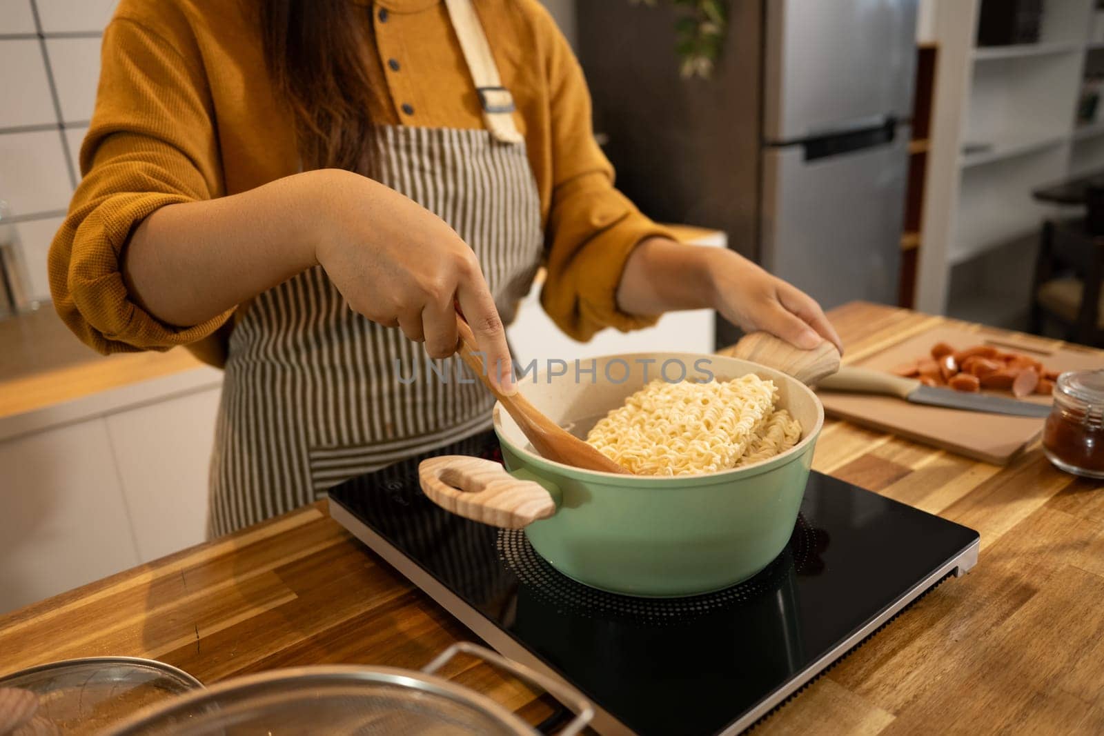 Close up shot of woman placing a block of instant noodles into a green pot.