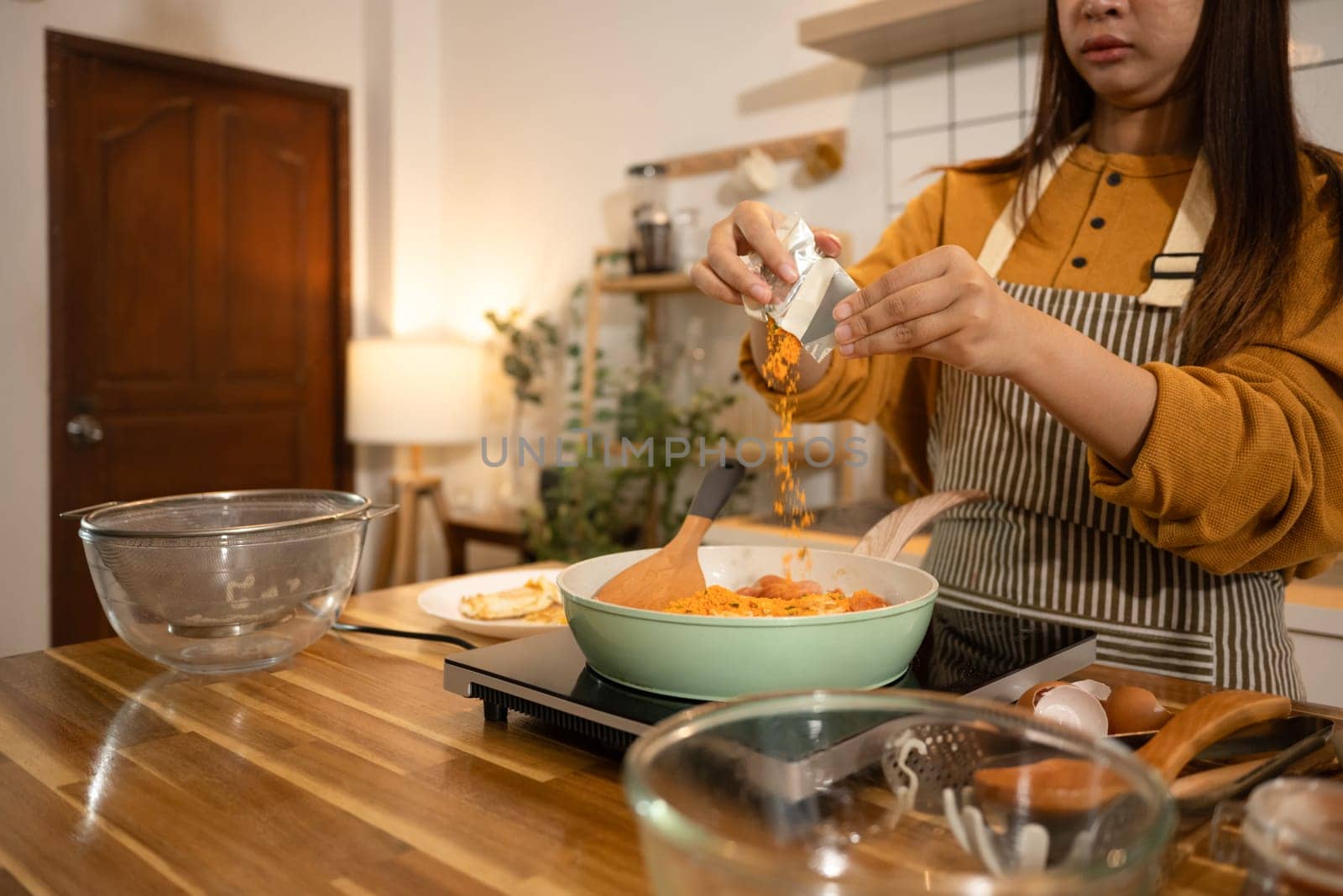 Shot of woman adding powdered seasoning to a pot of instant noodles and sausages.