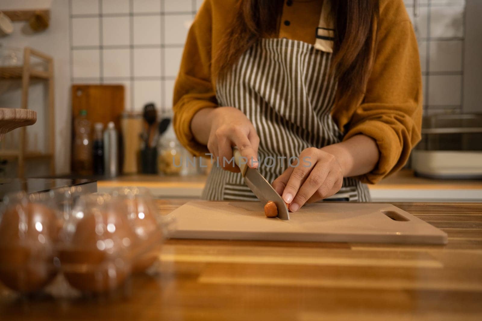 Close up woman chopping sausage on cutting board in a warm kitchen.