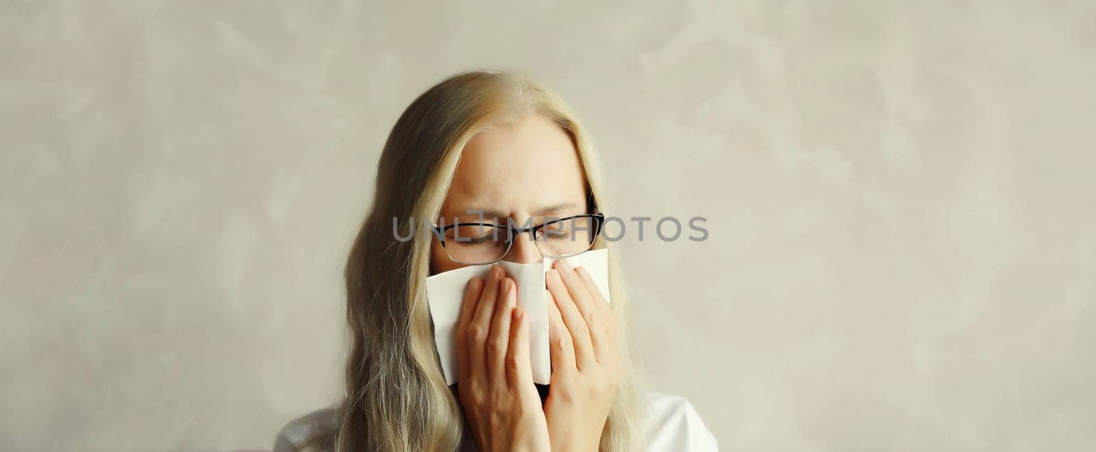 Sick exhausted mature woman sneezing blow nose using tissue, unhealthy suffering girl feels unwell at home