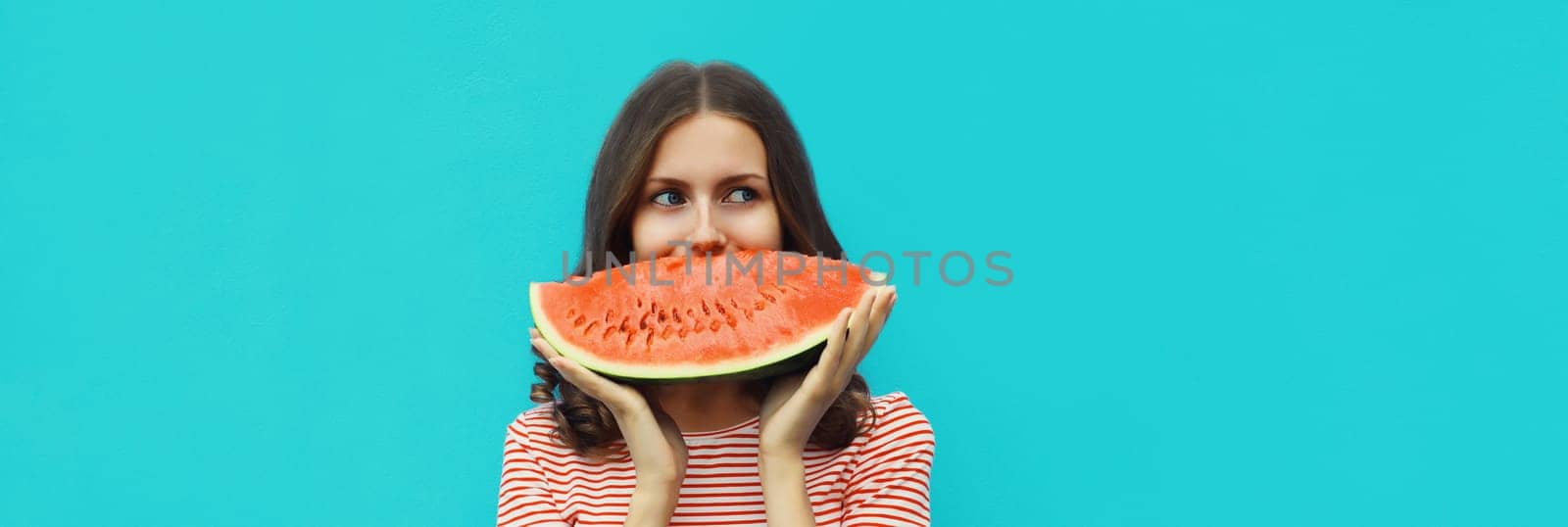 Summer portrait of happy young woman eating fresh slice of watermelon on blue studio background