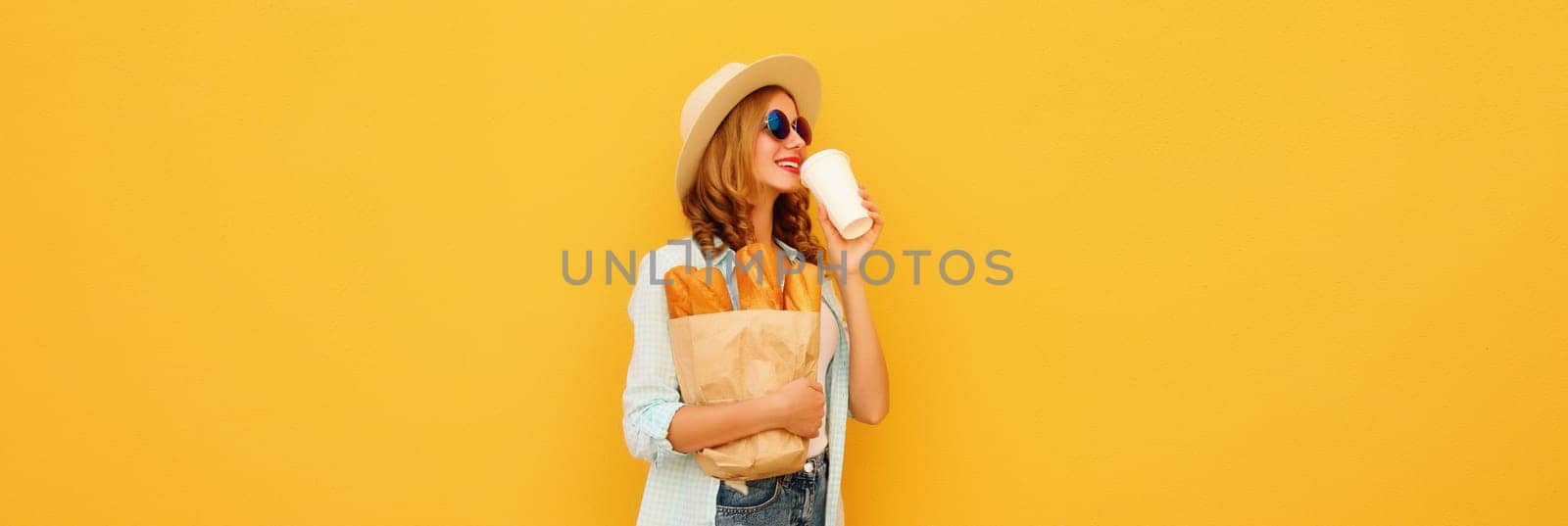 Happy modern bakery customer young woman holding grocery shopping paper bag with long white bread baguette drinking coffee on bright yellow background