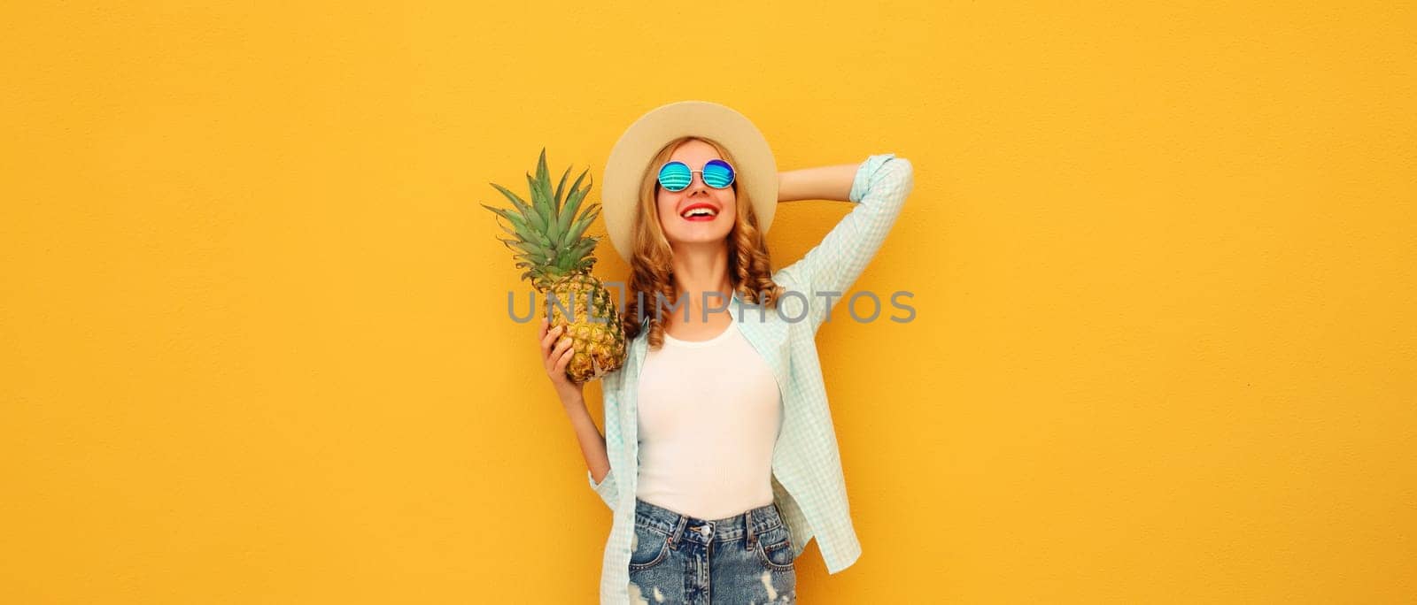 Summer vacation, happy joyful young woman with pineapple fruit in tourist hat, cheerful girl posing on yellow studio background