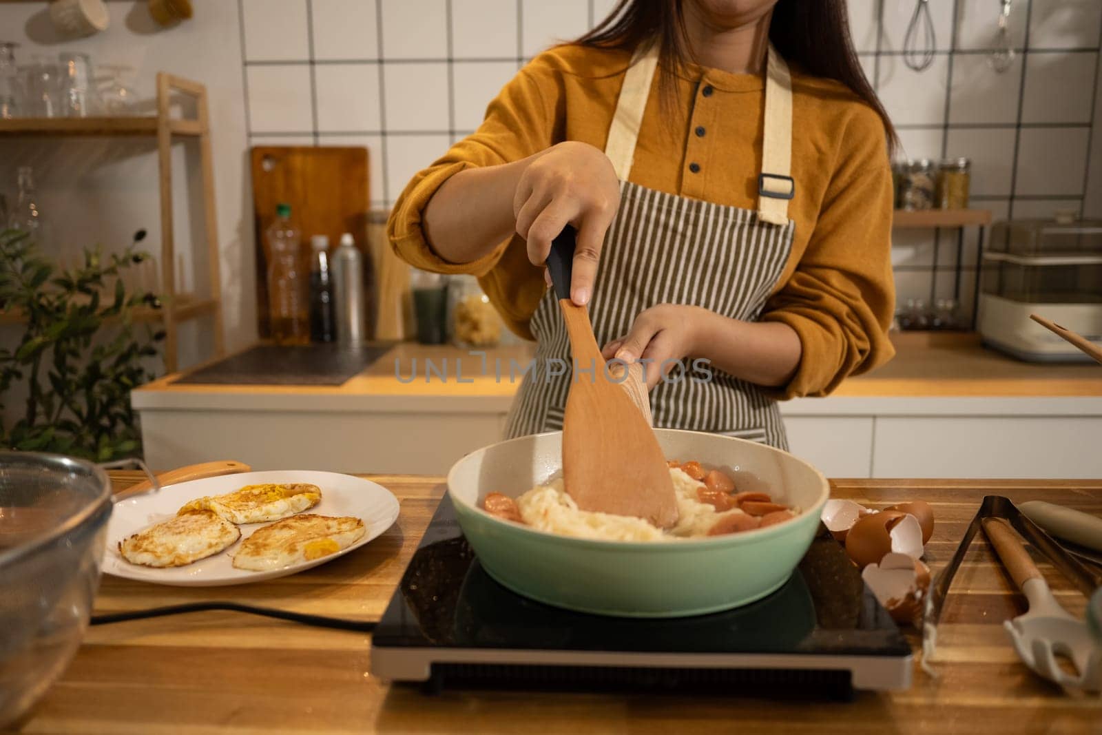 Young Asian woman preparing meal on an Induction stove in a kitchen.