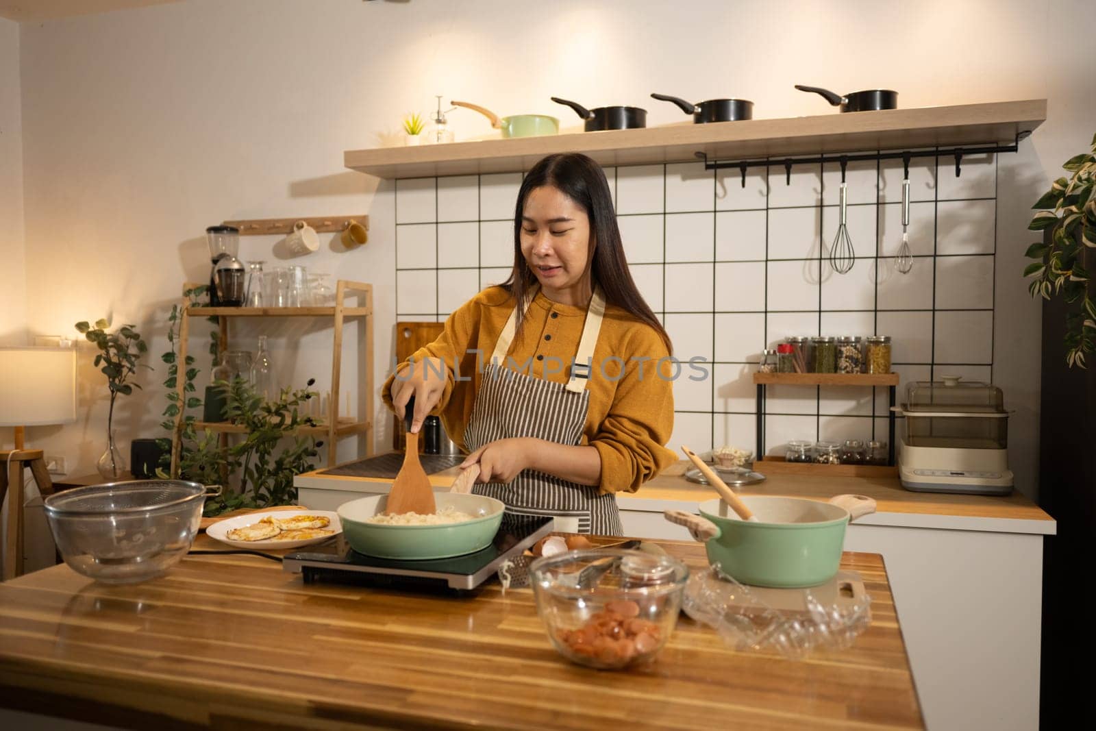 Smiling woman in apron stirring food in frying pan on an induction stove.