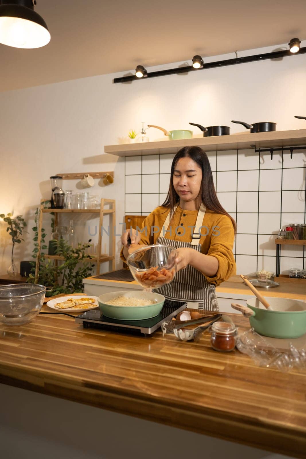 Young Asian woman preparing meal on an Induction stove in a kitchen.