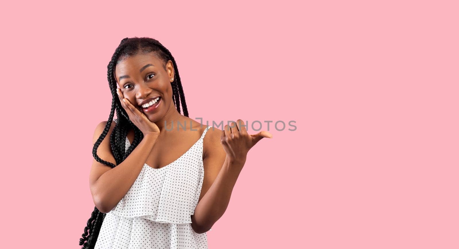 Summer sale. Emotional black lady pointing at blank space over pink studio background, banner design. Pretty African American woman in trendy clothes having special offer, advertising your product
