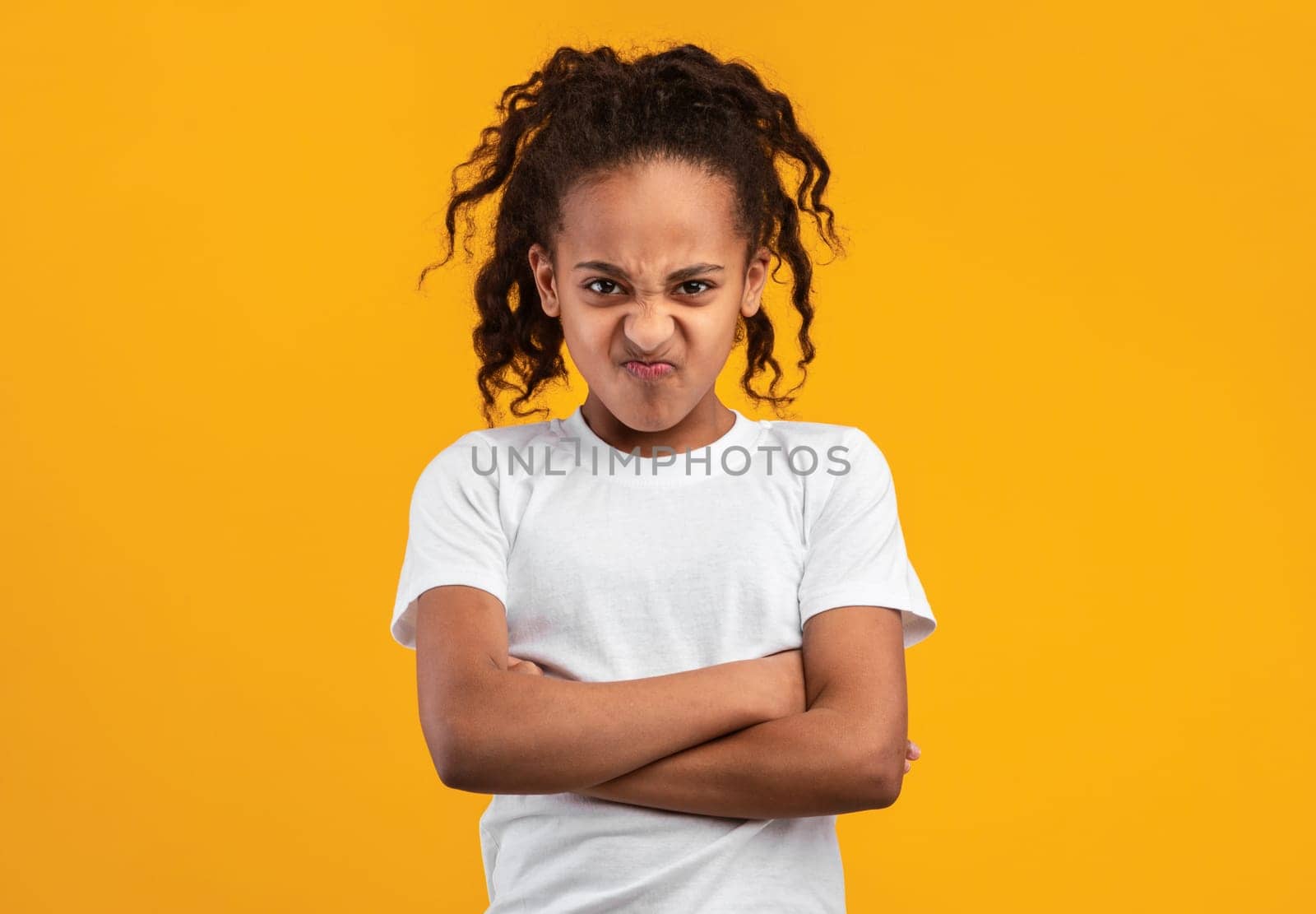 People Emotions, Teen Maximalism Concept. Portrait of offended young black girl posing with folded arms, standing isolated on yellow studio wall. Angry lady holding hands crossed, looking at camera