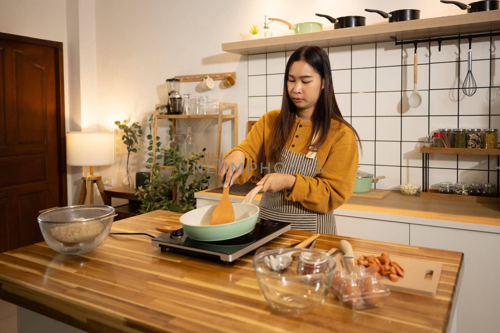 Young Asian woman preparing meal on an Induction stove in a kitchen.