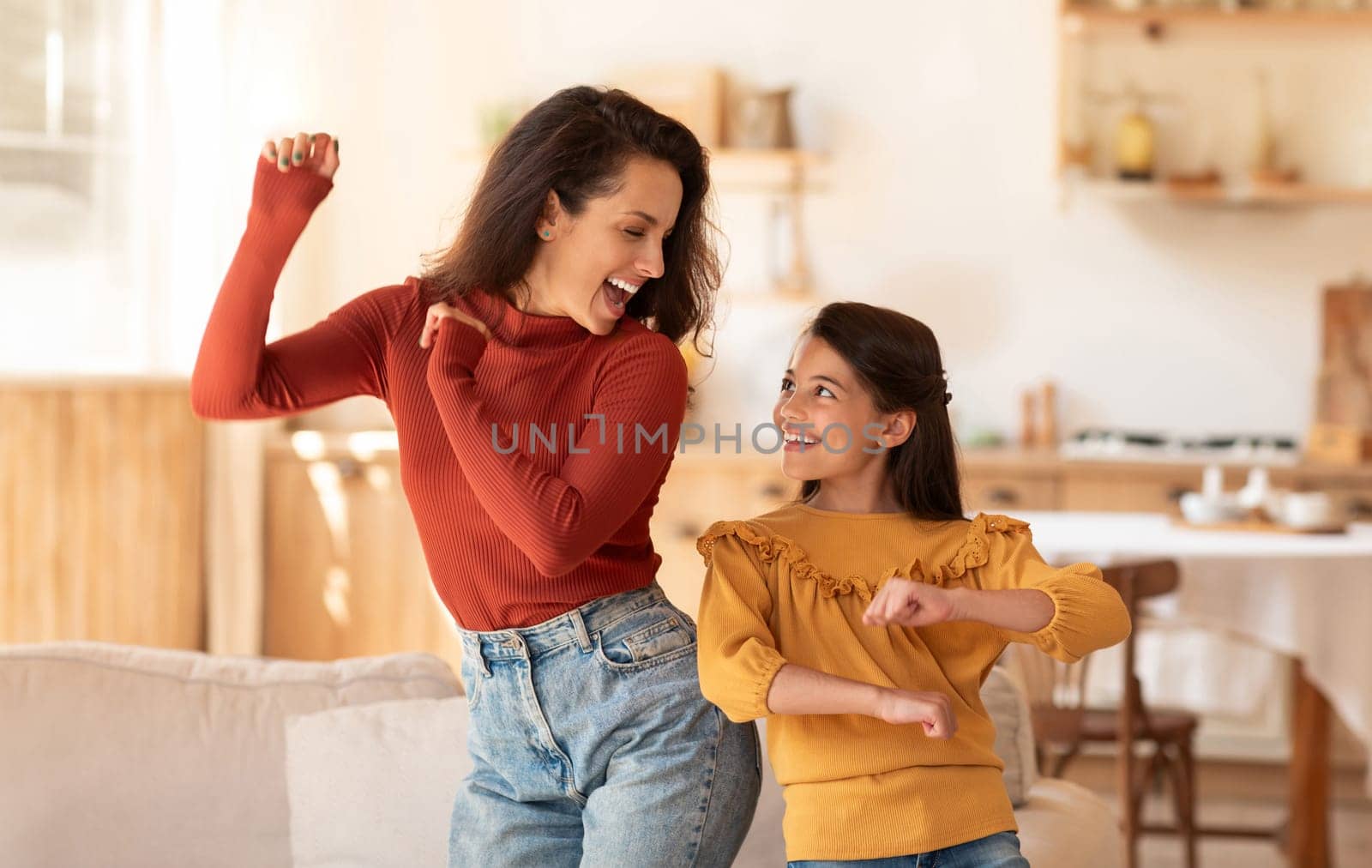 Cheerful Middle Eastern Mother And Daughter Kid Dancing Together At Modern Kitchen Interior. Young Mom And Preteen Child Girl Having Fun During Home Party Indoors On Weekend