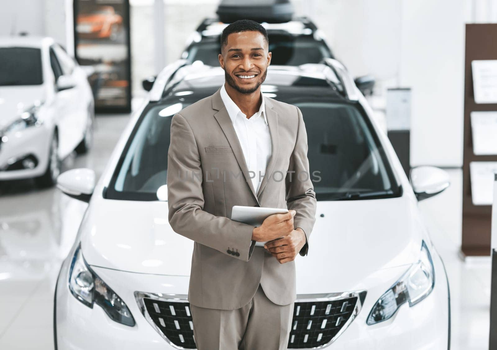 Cars Dealership Concept. Auto Seller Afro Man Smiling To Camera Standing In Automobile Center.