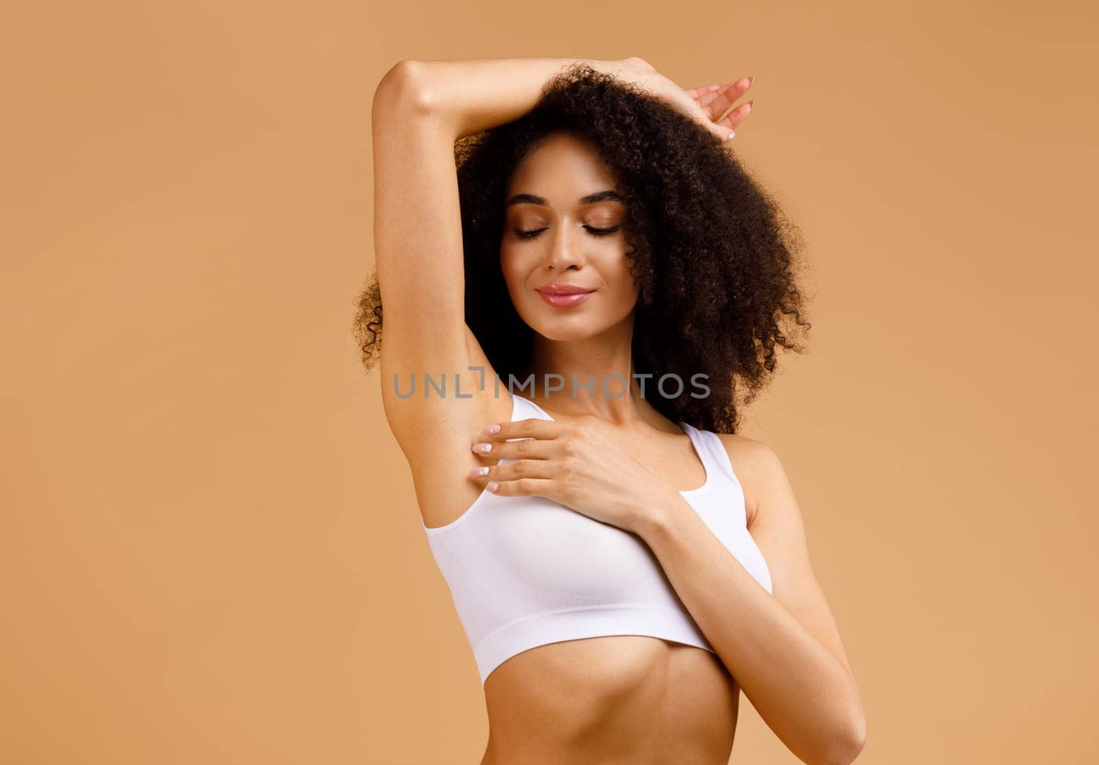 Young black woman with perfect soft armpit skin enjoying results of routine procedures, putting hand up, free space, advertisement for under arm deodorant and epilation, beige background