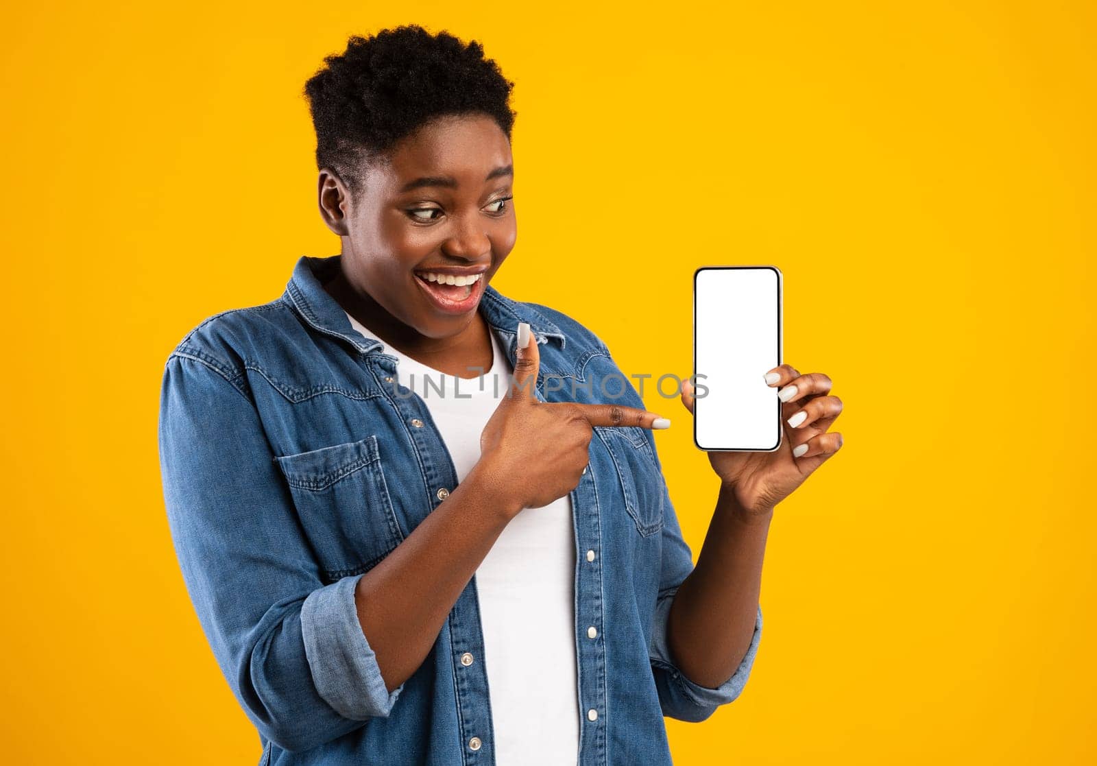 Cheerful Black Lady Showing Smartphone Blank Screen Recommending Application Posing Standing Over Yellow Studio Background. Mobile Application Ad. Check This App Concept. Mockup