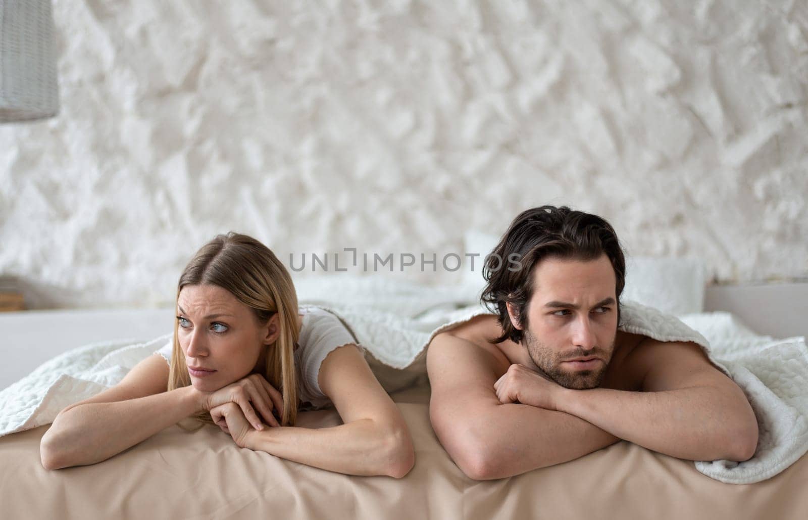 Sexual problems, relationship crisis. Stressed young couple lying in bed, overwhelmed with family difficulties, not speaking after conflict, suffering from erectile dysfunction or lack of libido