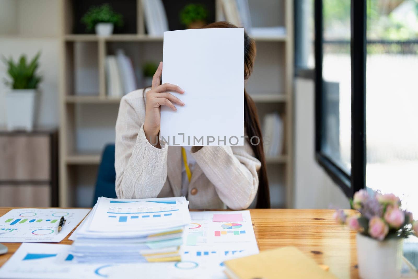 Stressed young businesswoman overwhelmed by paperwork with finance, market charts and documents in office.