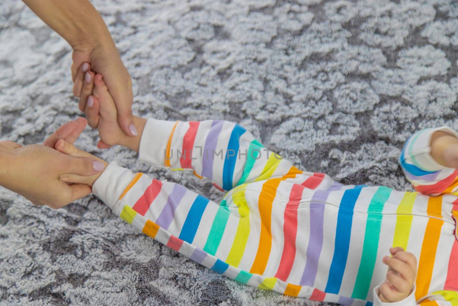A young mother massages her baby while playing with her on the bed. baby