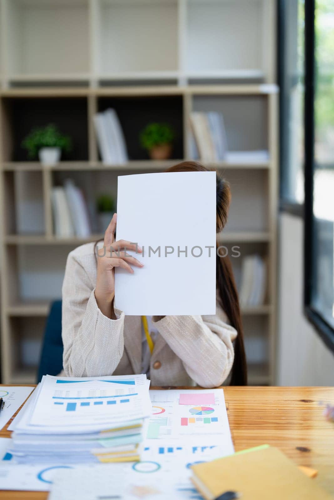 Stressed young businesswoman overwhelmed by paperwork with finance, market charts and documents in office.