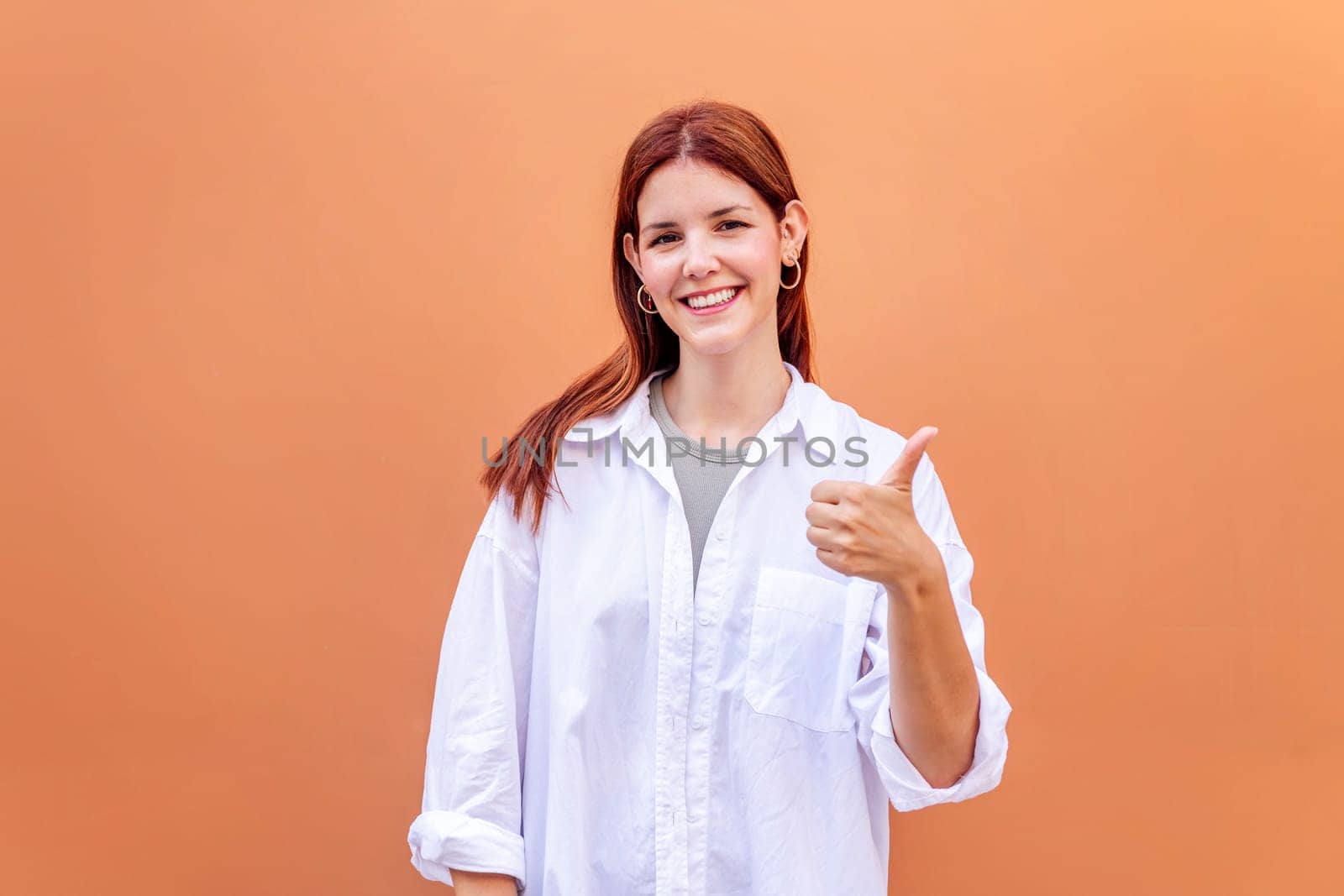 young woman giving a thumb up gesture while smiling looking at camera in a positive and friendly mood suggesting that she is happy and content, copyspace for text
