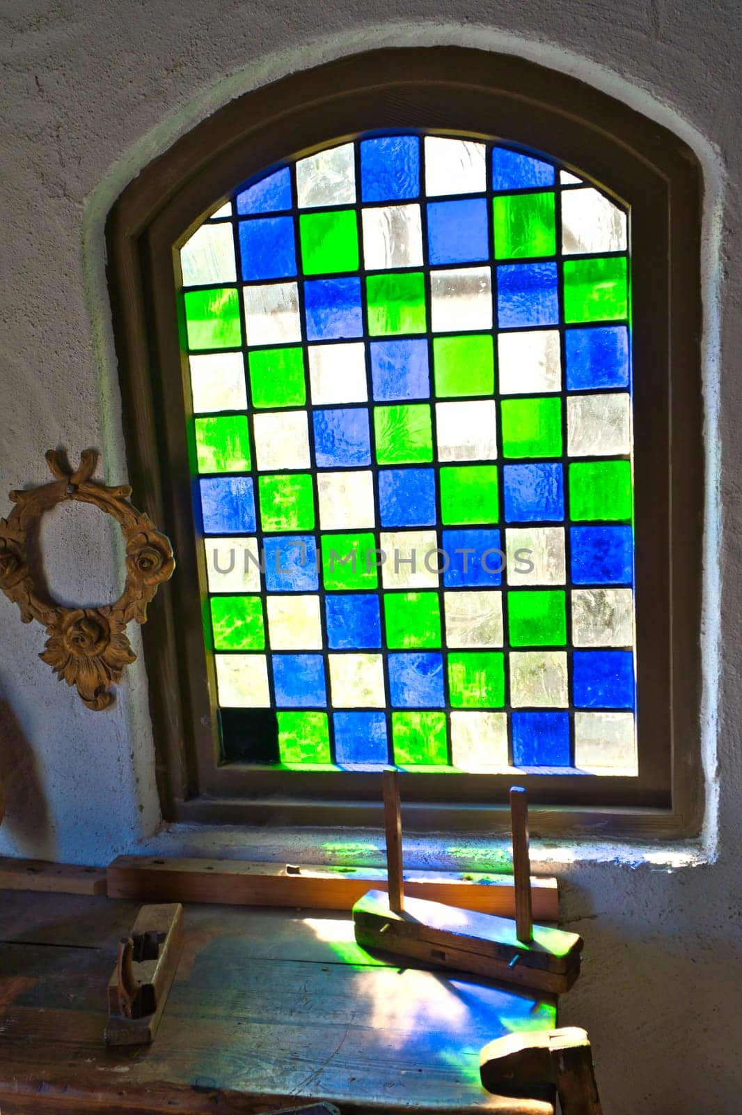 Colorful stained glass window in historical surroundings. Play of light on rustic wooden table with antique tools. Nostalgic atmosphere in vintage style
