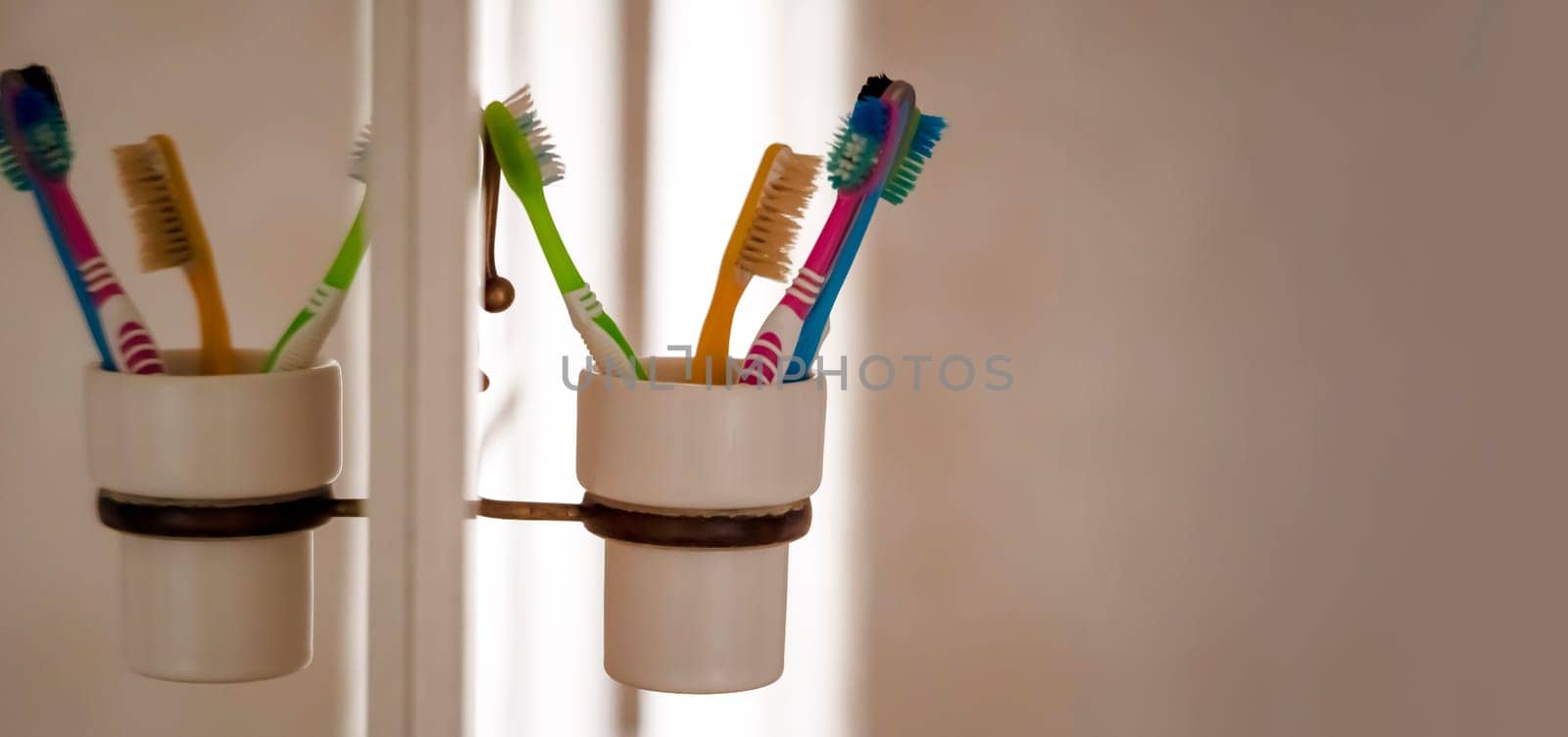 Toothbrushes in a glass attached to a mirror, personal hygiene products to take care of the cleanliness and health of the oral cavity, gums and teeth at home in the bathroom.