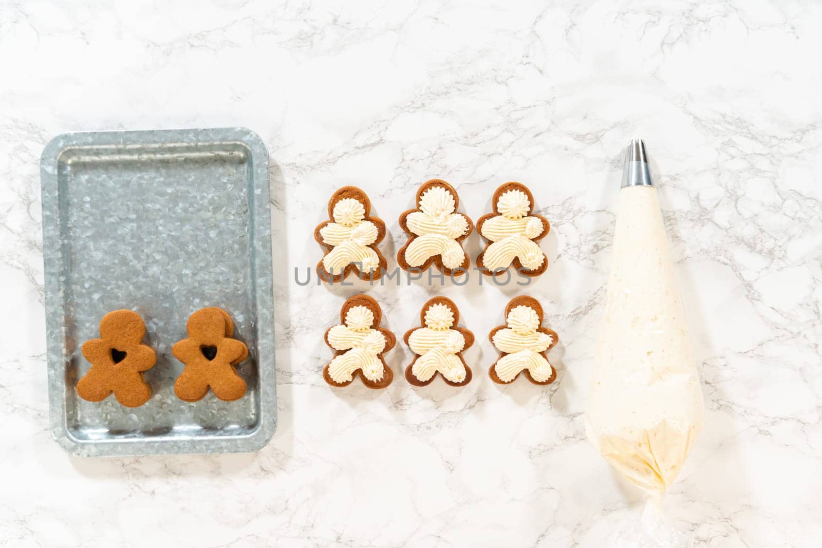 Flat lay. Gingerbread cookies await their second halves on a marble surface, each meticulously piped with buttercream to craft delightful sandwich treats. The precision of the piping adds a festive touch.