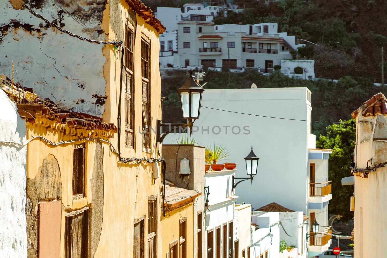 A beautiful picturesque street of the old town in the sun, houses with yellow and white walls, vintage windows and street lamps in a small village among the mountains.