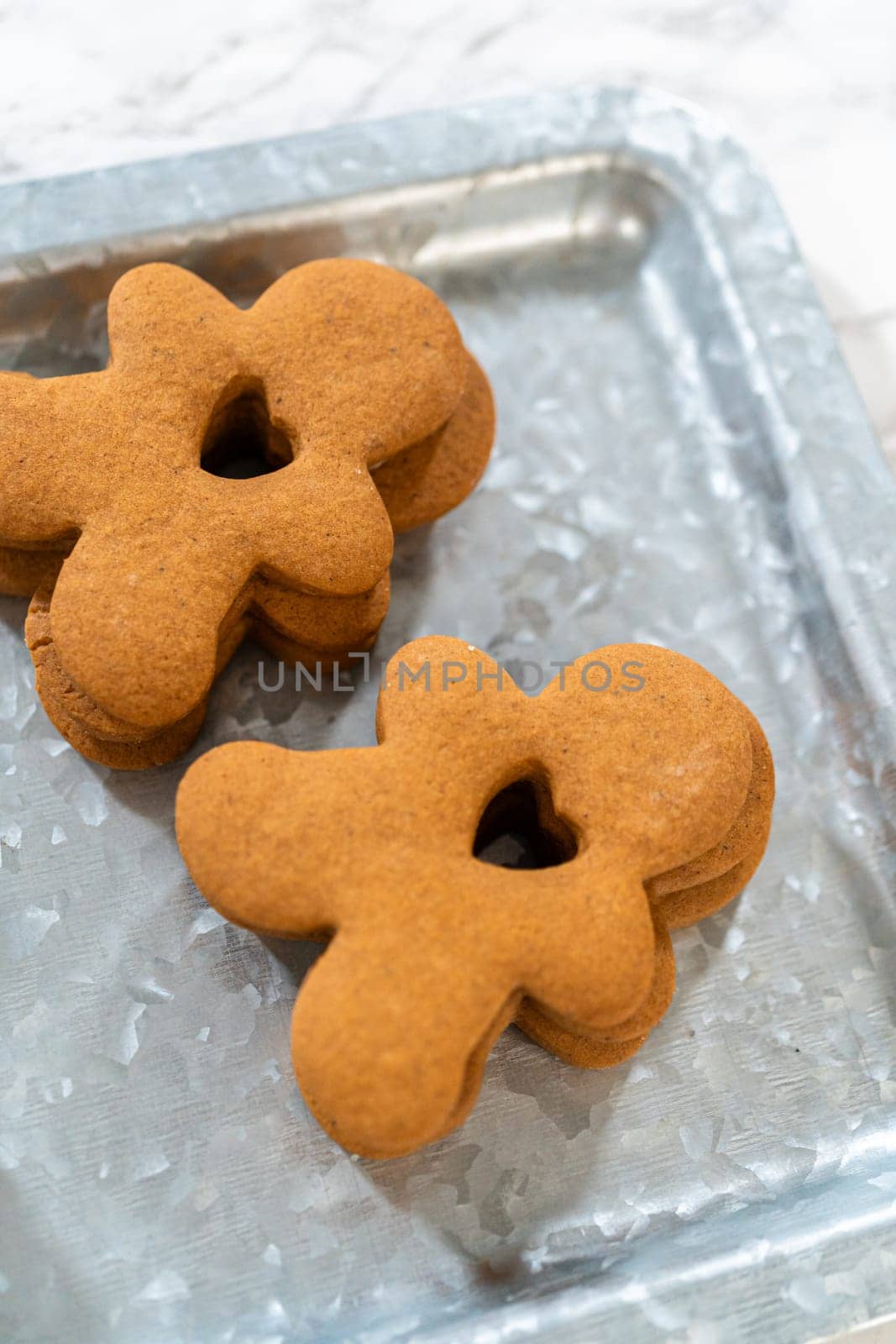 Gingerbread cookies, including a gingerbread man with a heart-shaped cutout, rest on a rustic metal tray against a marble countertop.
