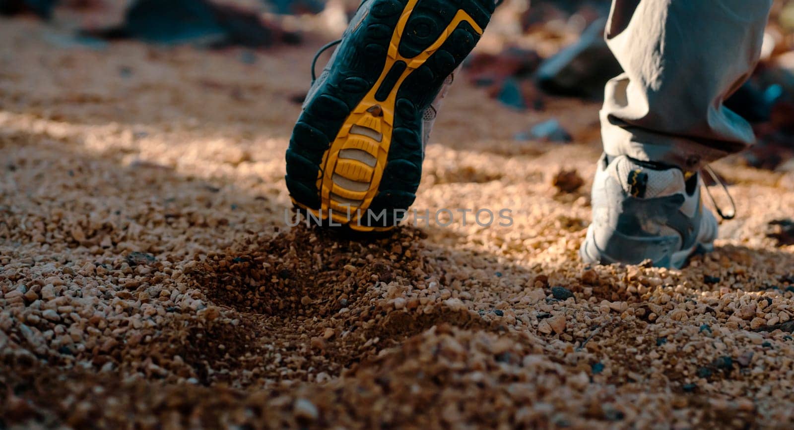 Male legs in trekking shoes close-up, a man walks along a trail among rocky mountains, hiking on a volcano, sand dunes at sunset.