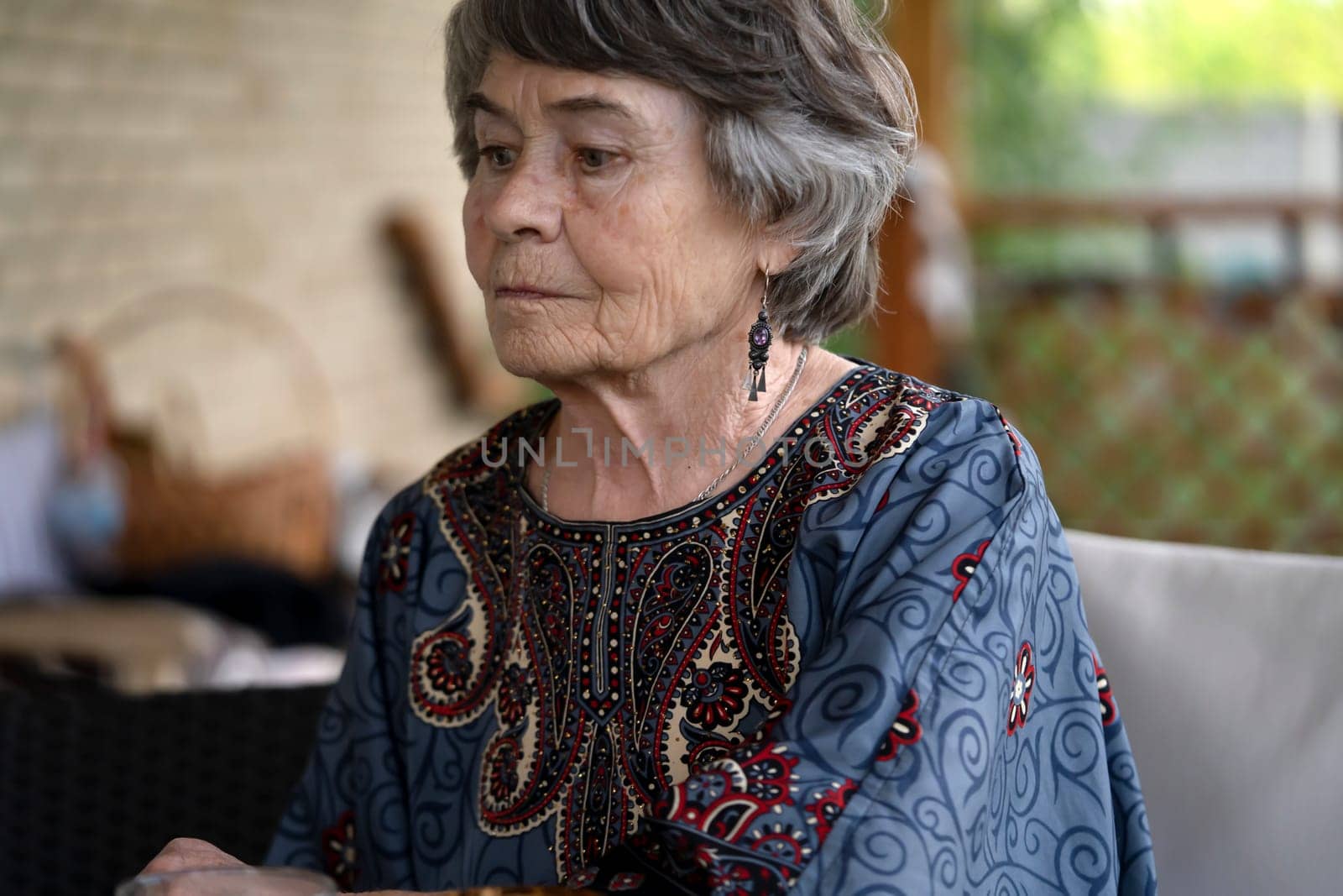 A beautiful elderly woman aged 80 with a smiling face sits on the veranda of her cozy house in a smart dress, a happy pensioner takes care of her beauty and health.