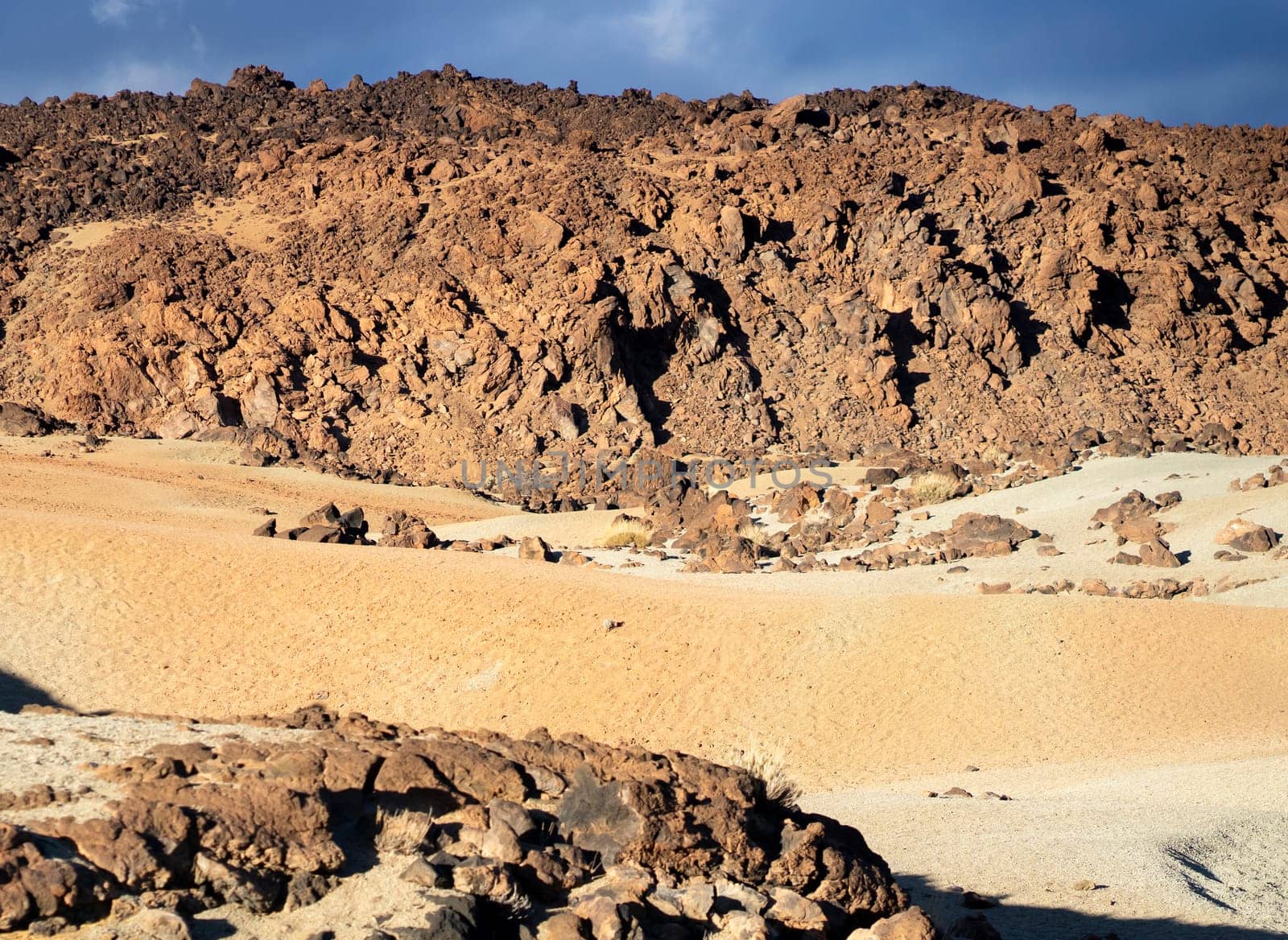 Volcanic lunar landscape in the sun with black lava formations, mountains and desert, red golden sand. Scenic dramatic view with volcanoes and rocks at sunset.