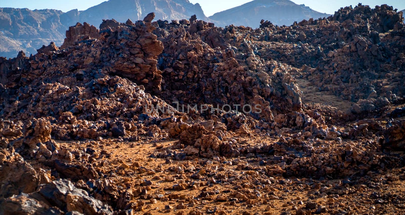 Volcanic lunar landscape in the sun with black lava formations, mountains and desert, red golden sand. Scenic dramatic view with volcanoes and rocks at sunset.