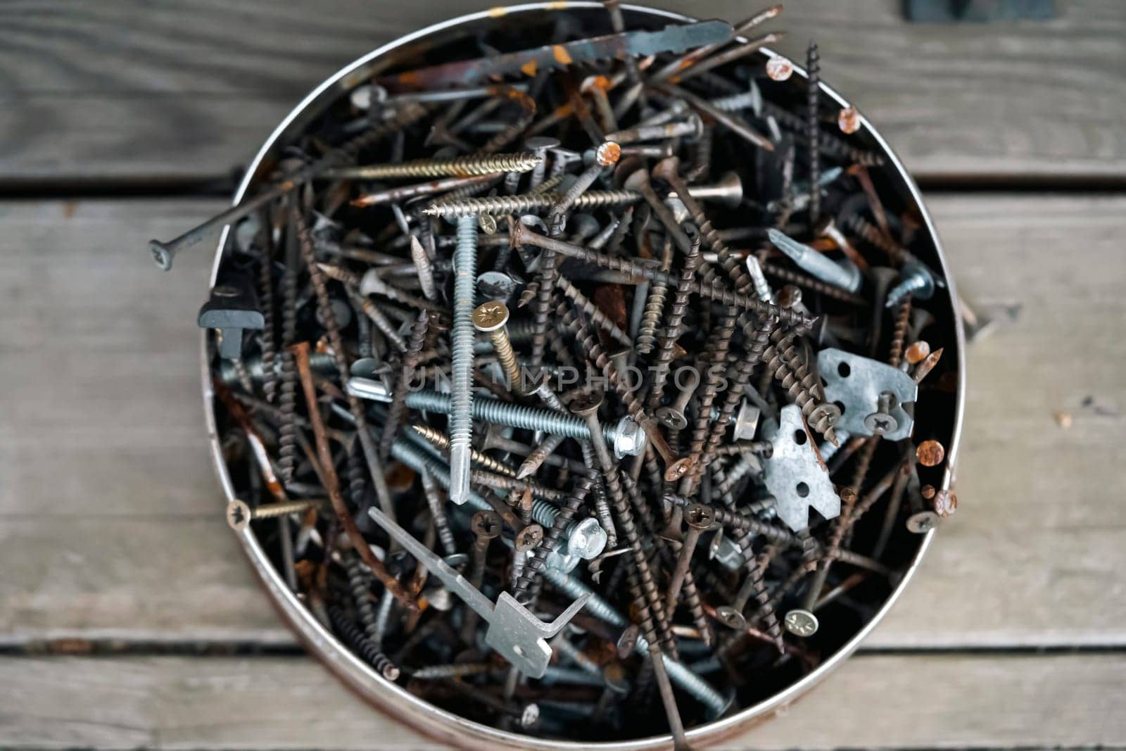 Old vintage nails in a round box lie on the porch of a wooden country house, top view. Old things for workshop and recycling and creative work.