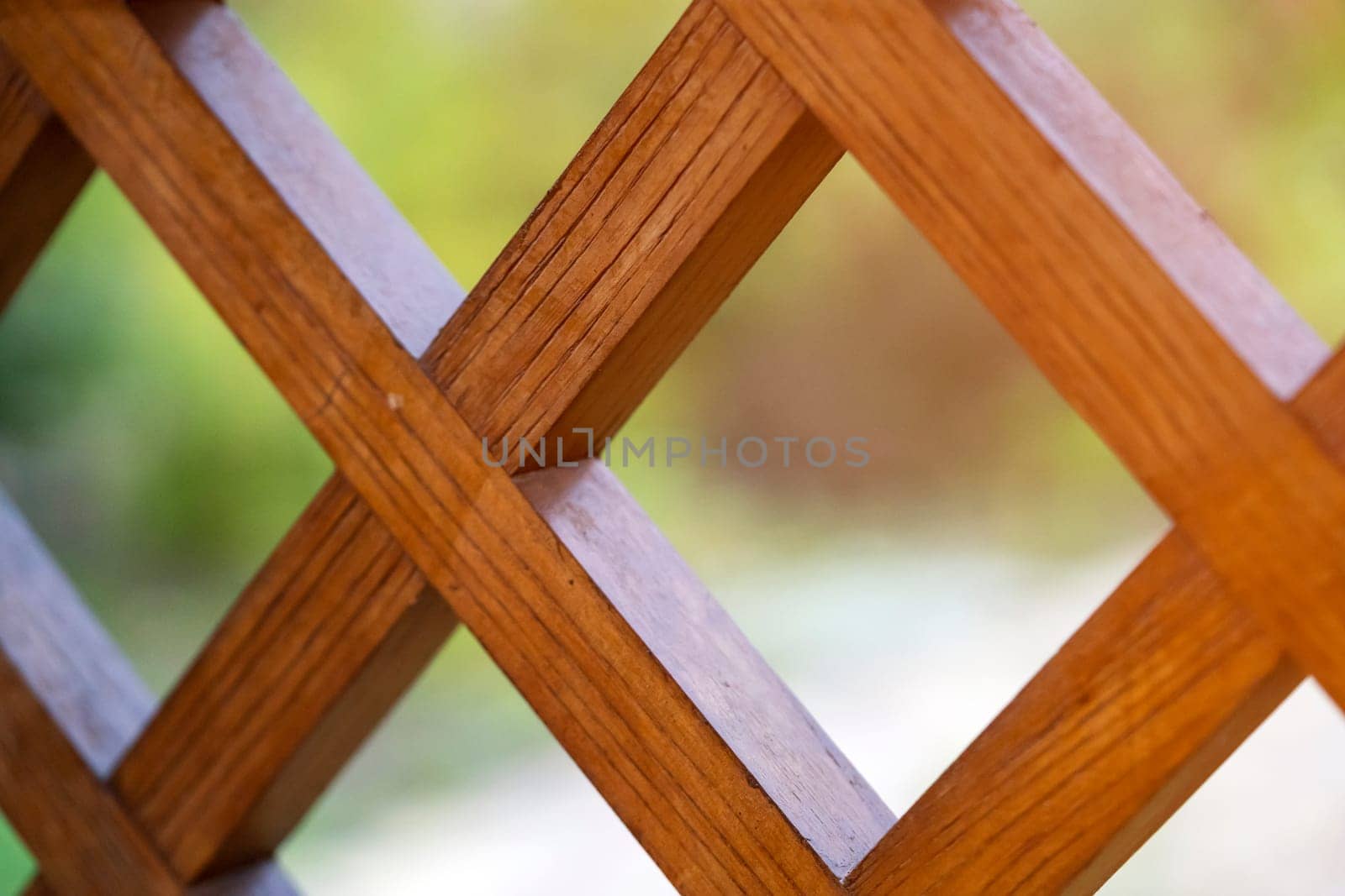 A beautiful background with a wooden lattice, a square grid, a decorative fence on a balcony or terrace against the backdrop of a summer garden, an outdoor fence with a square, rhombic pattern.