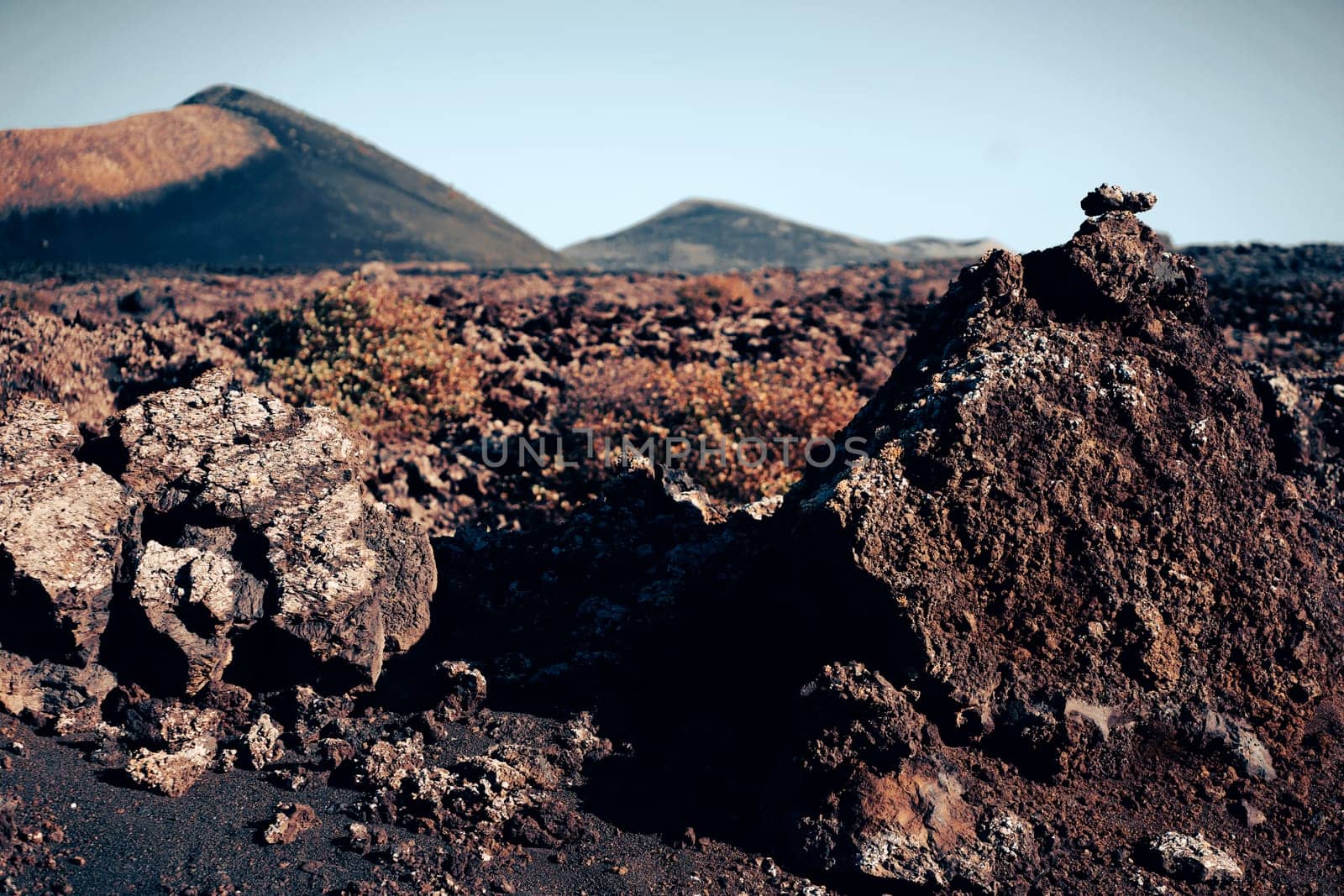 Volcanic landscape with fossilized dark lava, stones, rocks, mountains and volcanoes in Lanzarote National Park, Canary Islands.