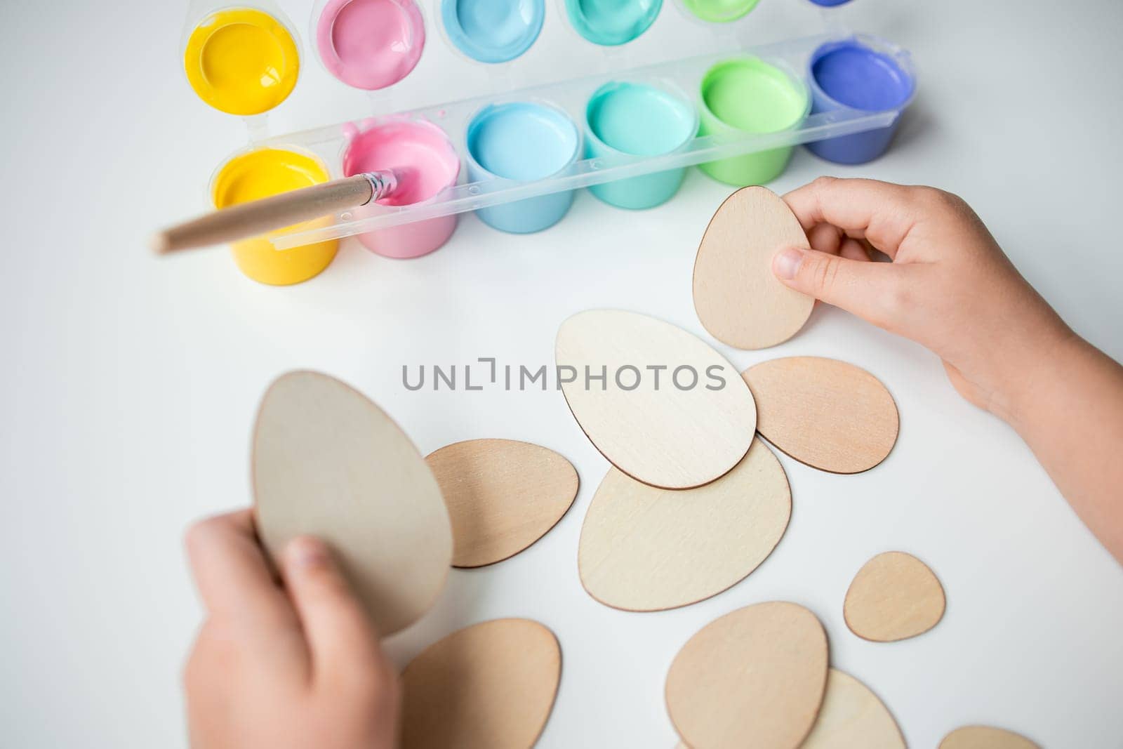 Child painting wooden Easter eggs with colorful paints.