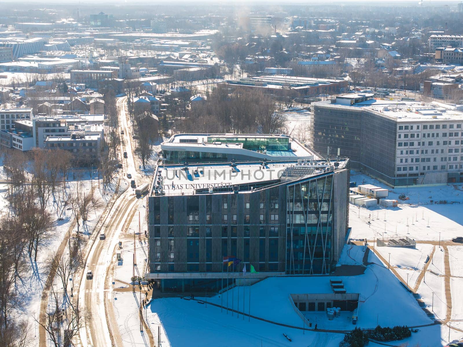 Aerial view of Riga, Latvia, showcasing the modern University of Latvia building with glass facades, snow covered streets, and a sprawling cityscape.