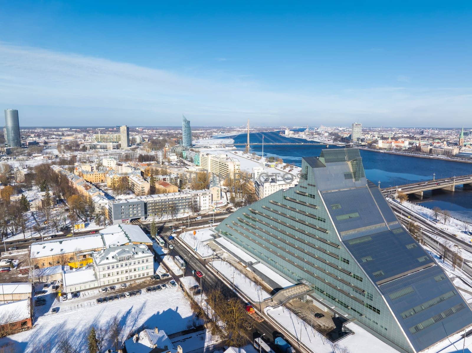 Aerial view of Riga, Latvia, featuring the National Library, Daugava River, a bridge, and a skyline of historic and modern buildings in winter.