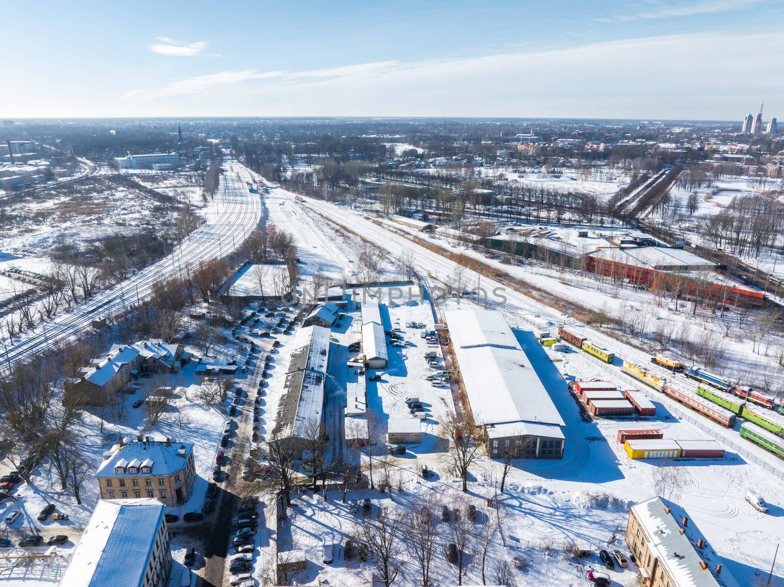 Snow covered Riga, Latvia, with the Train Museum's colorful train cars, industrial buildings, and rail tracks extending into the distance.