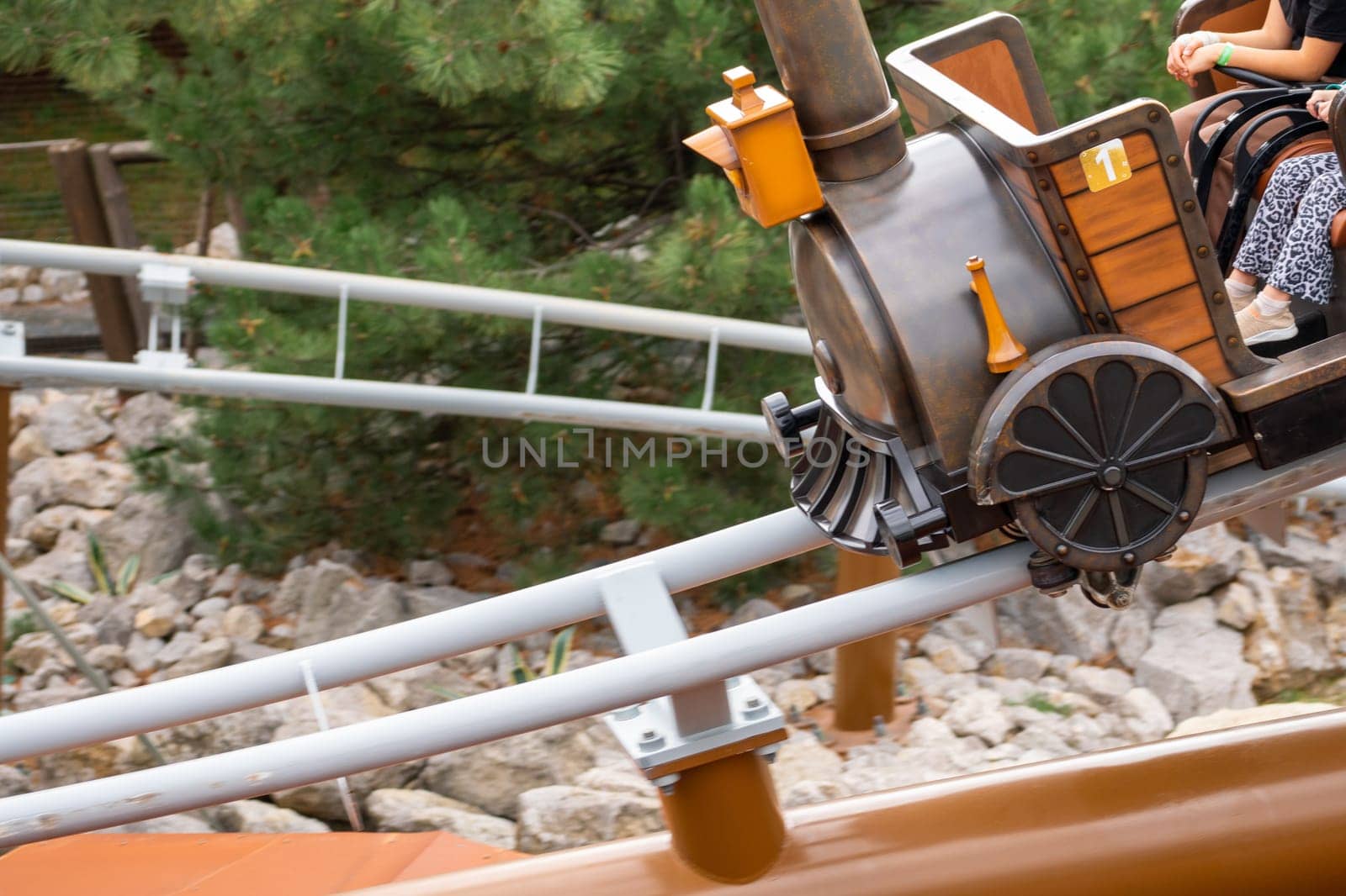 A miniature train with a wooden cart, carrying a passenger, navigates a sharp bend on a rollercoaster track.