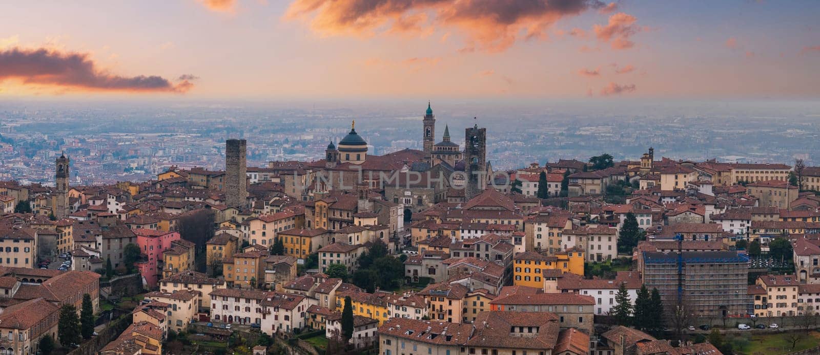 View of Bergamo's old town, Italy, at sunset, featuring the Basilica of Santa Maria Maggiore, medieval bell towers, and terracotta rooftops.