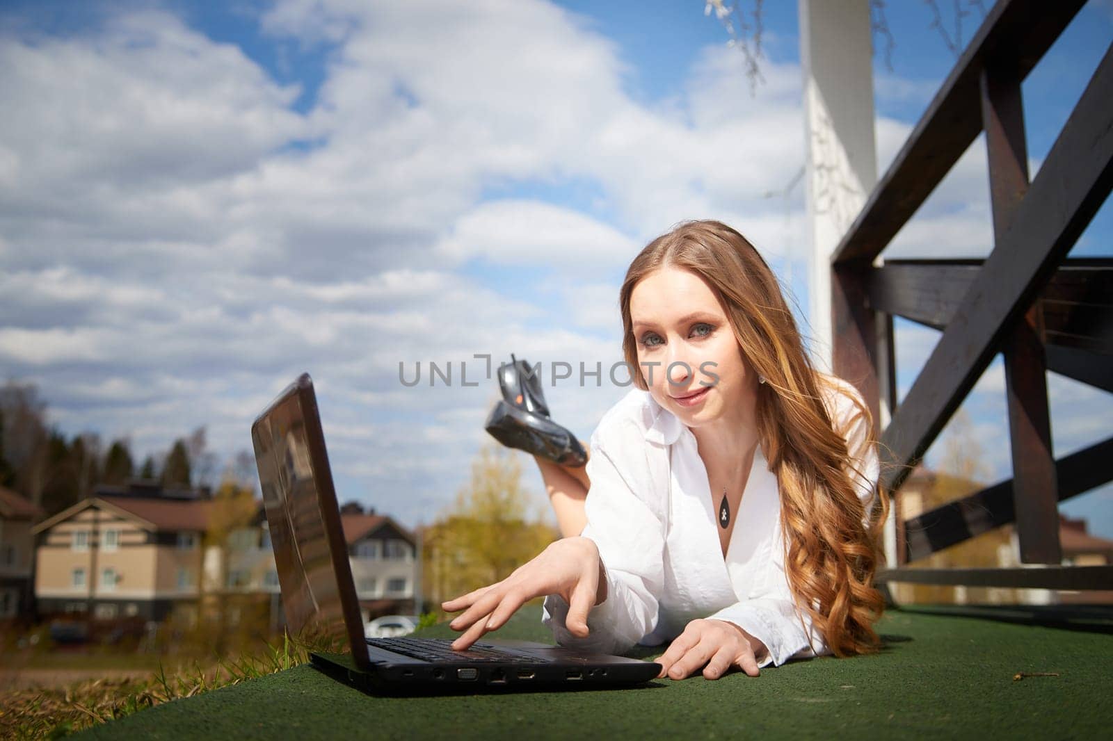 A woman is lying on the ground using a laptop, enjoying the sunny weather in a urban setting.