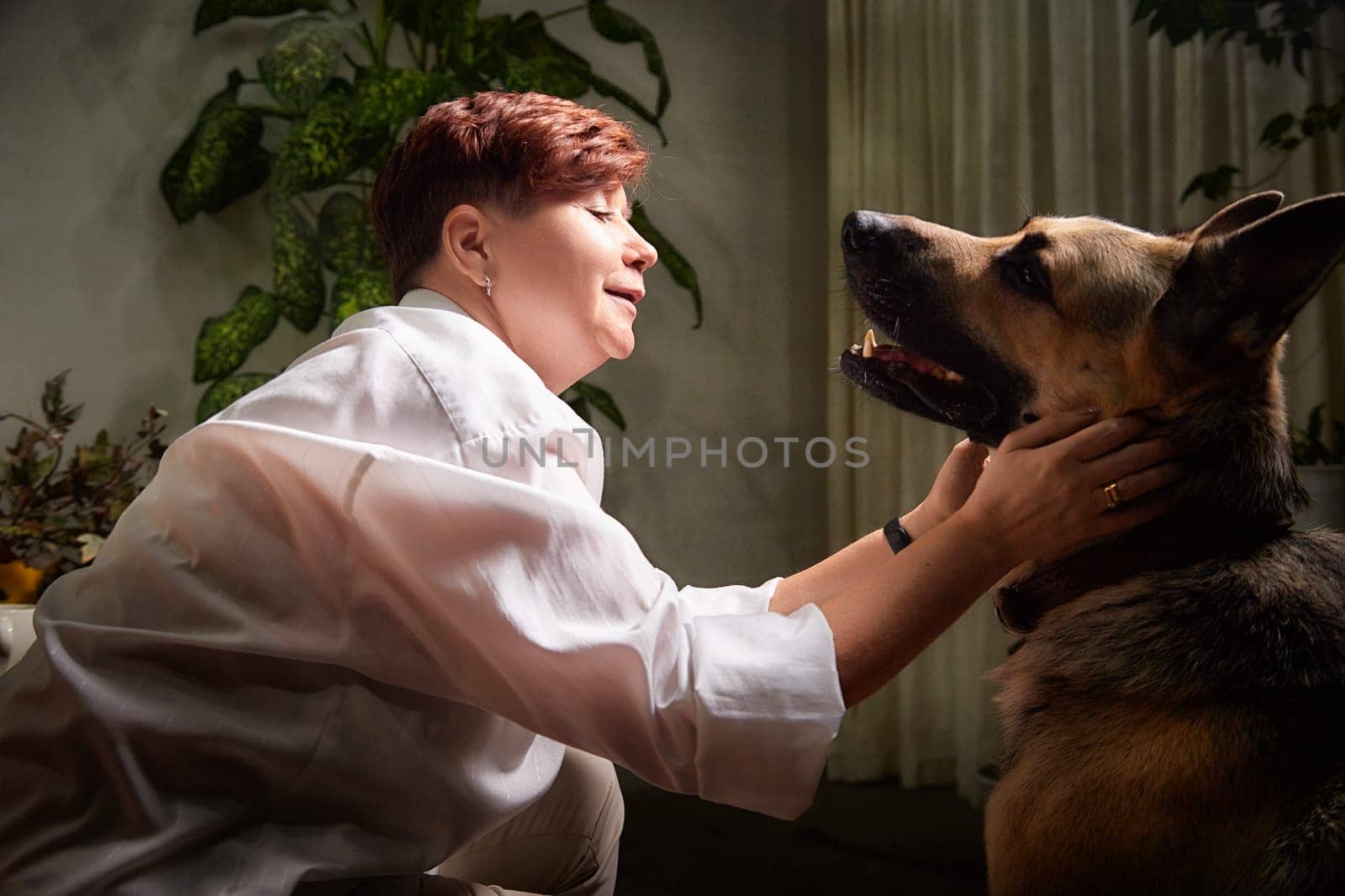 In a cozy room, a middle-aged woman shares a warm bond with her German Shepherd, embracing her pet lovingly.