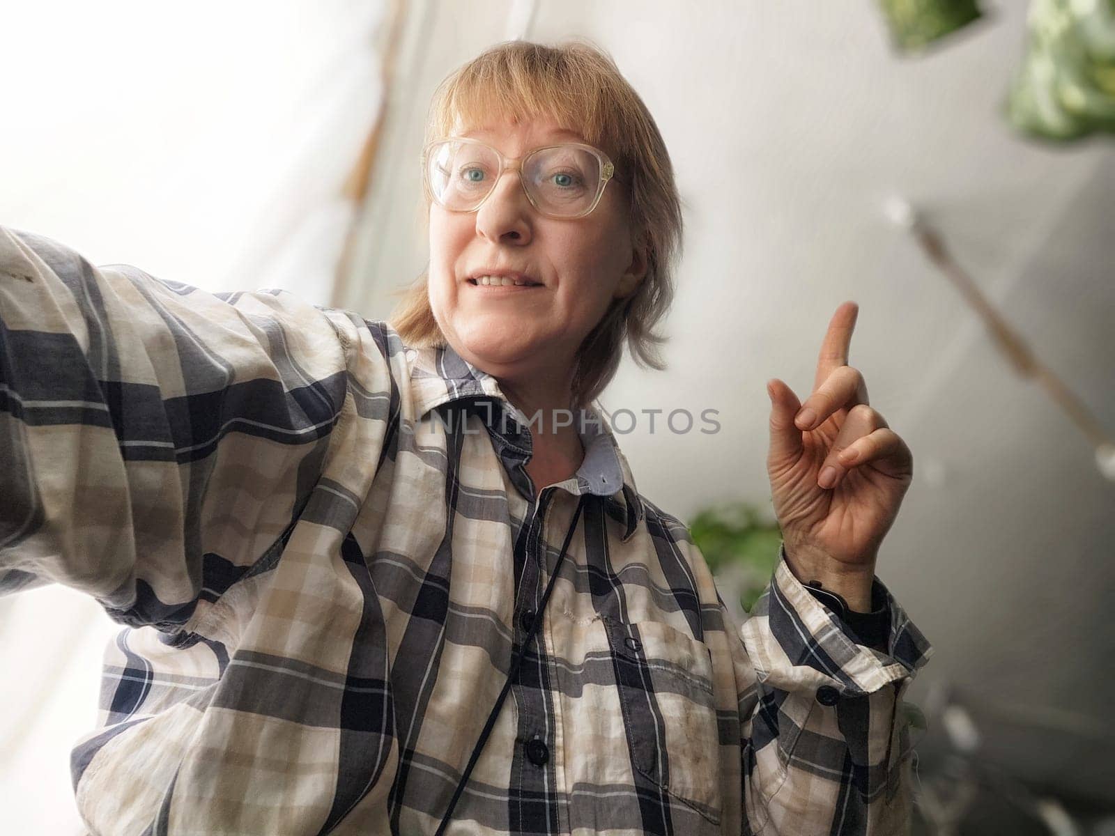 A mature woman with blonde hair smiles while taking a selfie in her cozy indoor space, sharing her thoughts on lifestyle blogging.