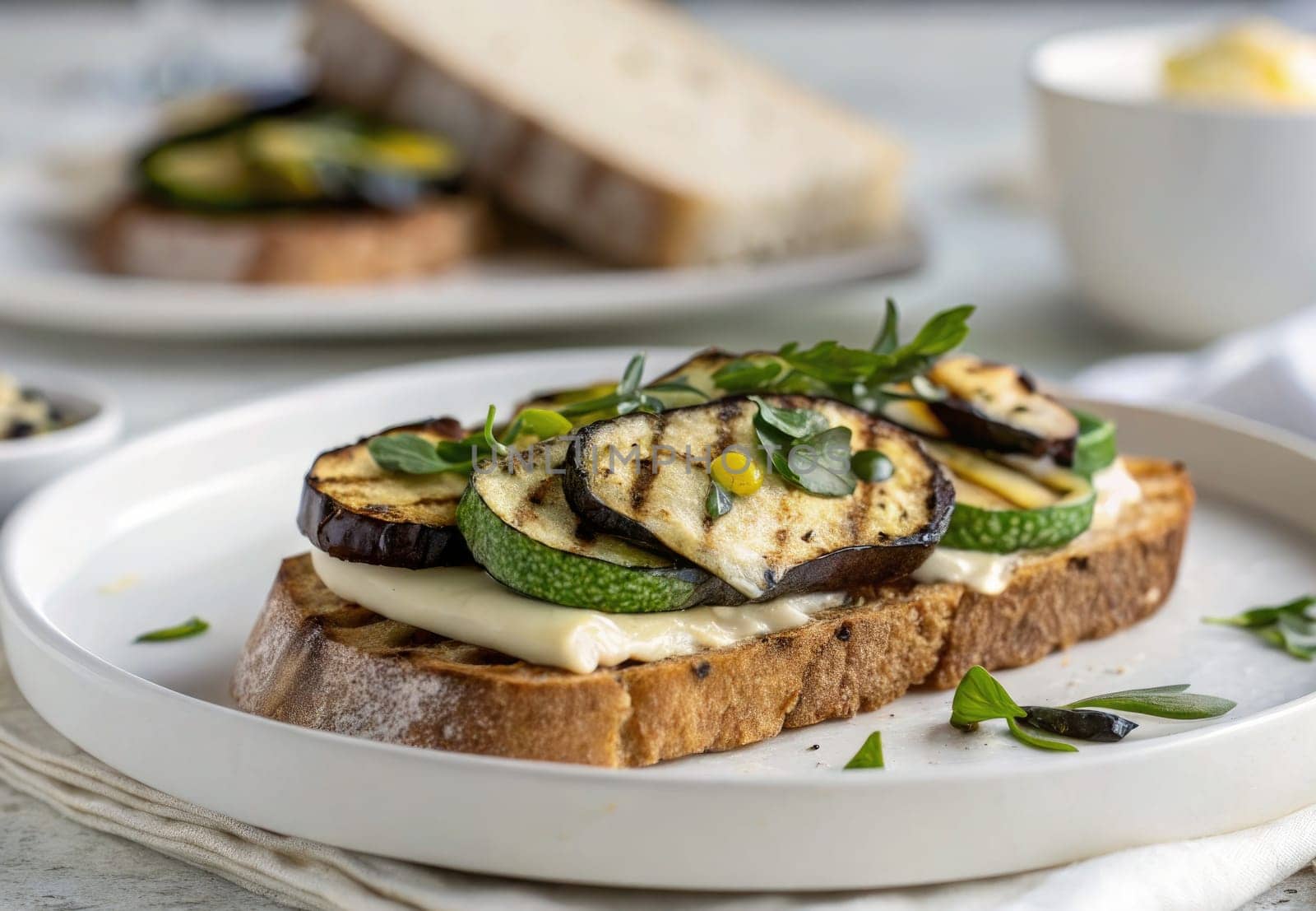 Toasted bread is topped with grilled zucchini, eggplant, and fresh herbs, served in a warm atmosphere. The dish is complemented by a creamy sauce, creating an appetizing meal experience.
