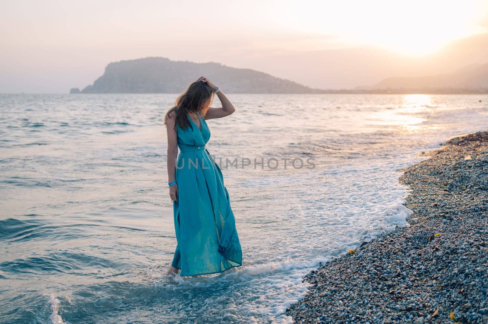 A woman in a flowing green dress poses on a pier by the sea at sunset, with a Turkey flag waving in the background.