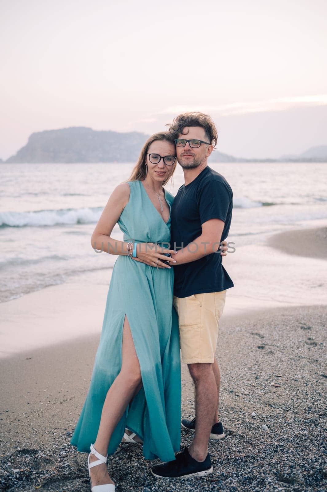 A smiling couple shares a joyful moment on the beach at sunset, the man and the woman near the sea waves, Alanya, Turkey